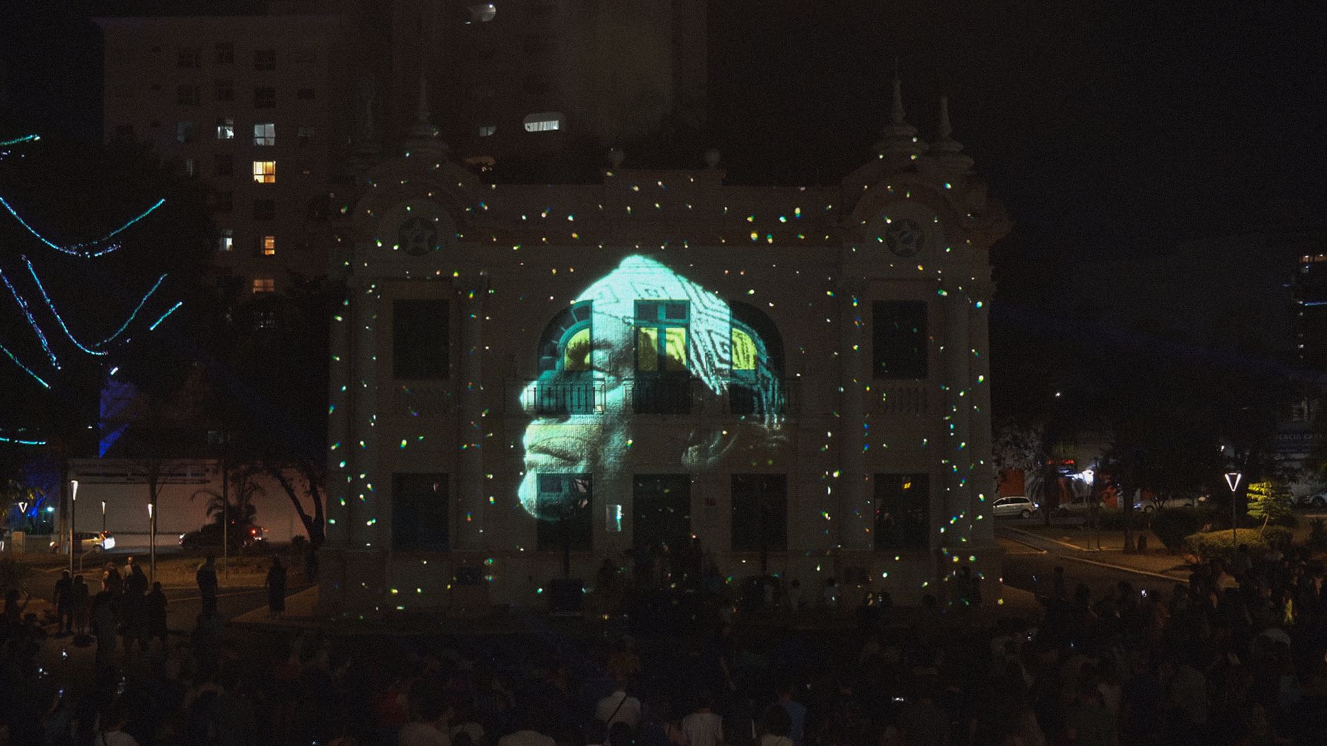 Rosto projetado na fachada do museu, à noite, com público